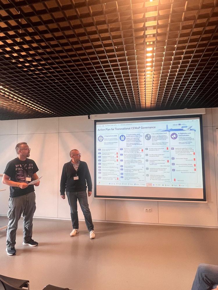 Two people standing next to a screen with a slide during a presentation